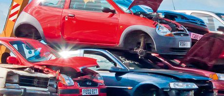 Car scrapyard with stacked cars and a crane lifting a vehicle.