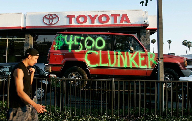 A man walking past a Toyota dealership with a red vehicle
